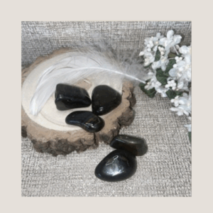 Blue Tiger’s Eye crystals on a wooden display with a white feather and flower, showing natural blue-gold banding.